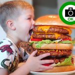 Large stand with child biting giant burger replica attracting customers for photos