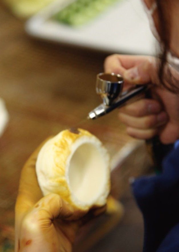 Japanese food replica artist using airbrush to paint each detail of a realistic model, matching the original dish photograph