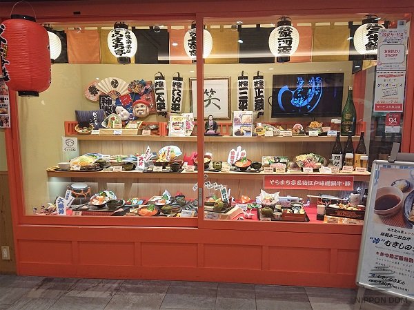Japanese cultural items are located in sushi restaurant display window: masks, dolls, hand fans, lanterns, pictures.