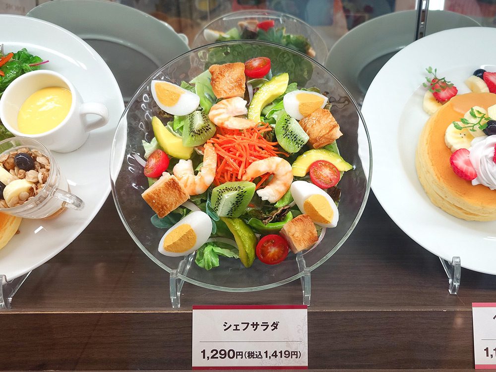 Close-up of a food replica price tag in the Japanese standard format — Chef Salad name and tax-inclusive price 1,290 yen below a salad replica