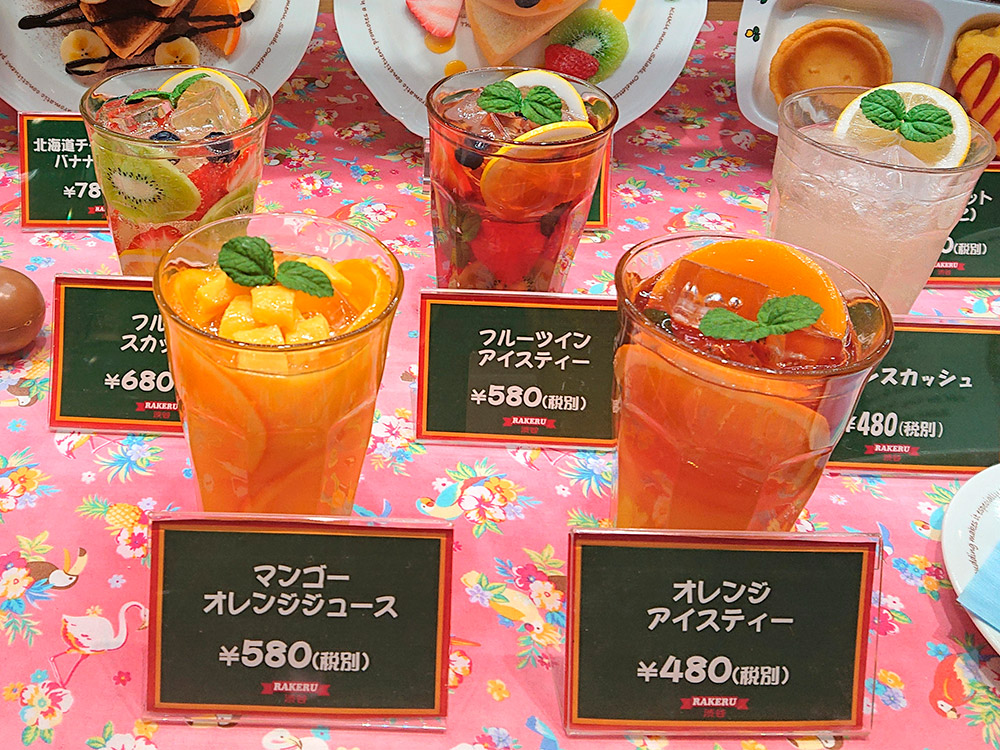 Row of drink replicas with name and price cards in a beverage window display