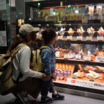 Dessert window displays at a cafe entrance with a mother and child stopping to look