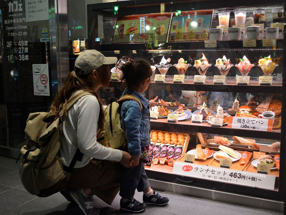 Dessert window displays at a cafe entrance with a mother and child stopping to look
