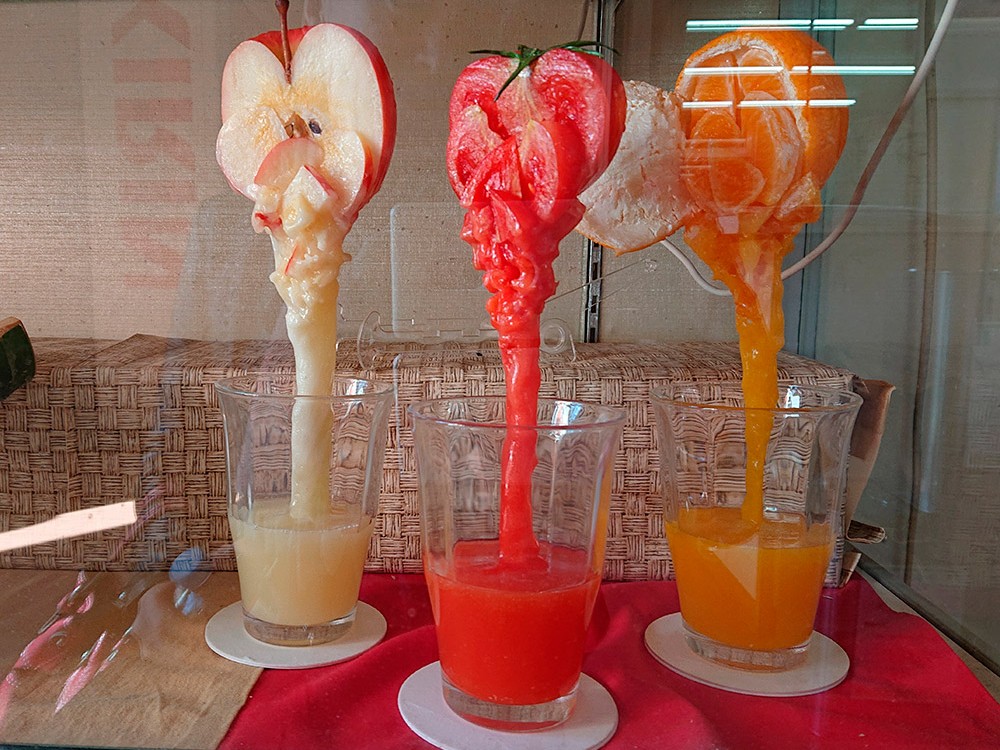 Apple, tomato and orange juice replicas pouring from whole fruit, cafe window drinks