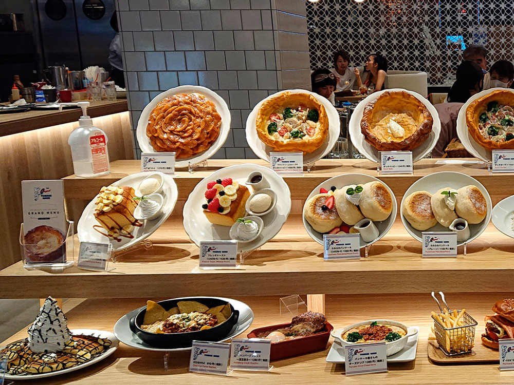 Dessert and dish models arranged on three wooden levels in a cafe window