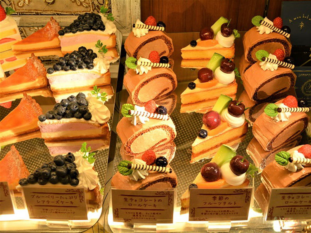Repeated cake slice models on mirrored trays filling a patisserie display case