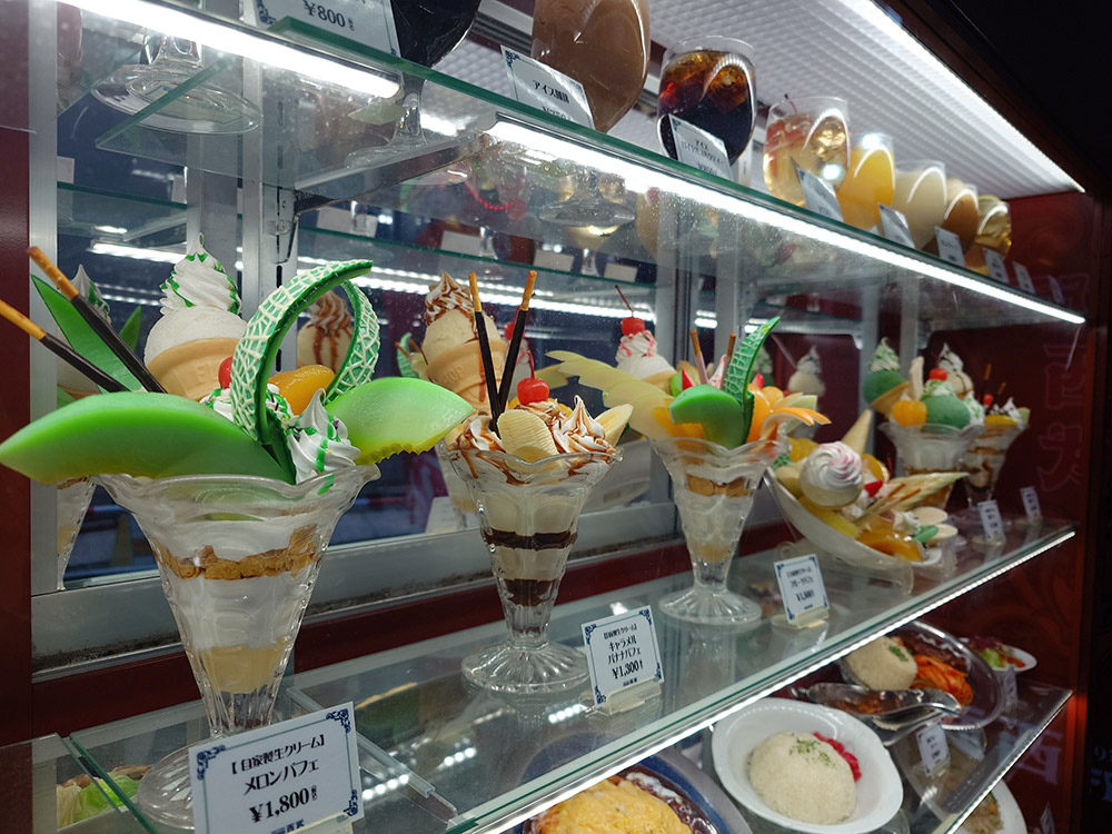 Dessert window display design with melon parfait models on LED-lit glass shelves