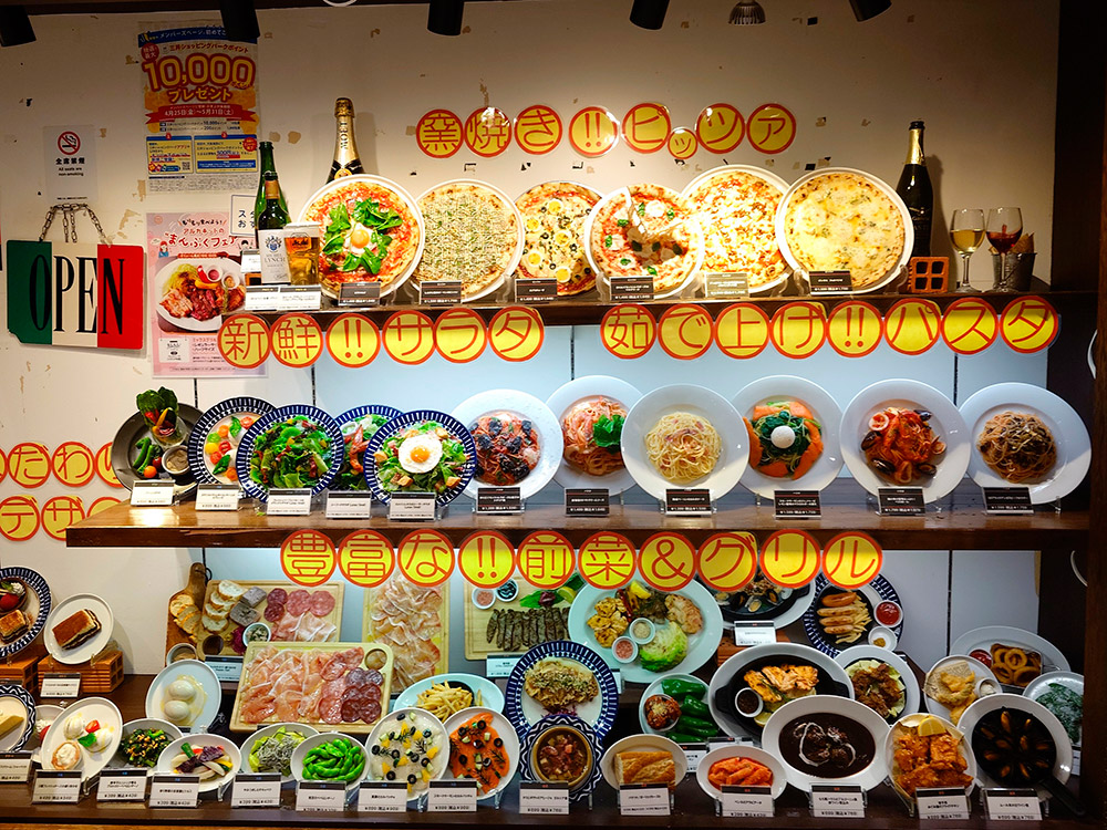 Pizzeria window displays with price cards and dish names under every food replica