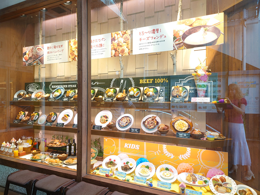 Replicas grouped by category on shelves: hamburger steaks, gratins, bread with drinks, kids meals