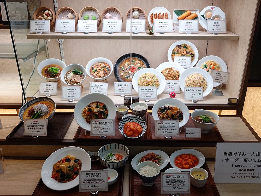Restaurant window display lighting reaching only the upper shelves of a Chinese food case