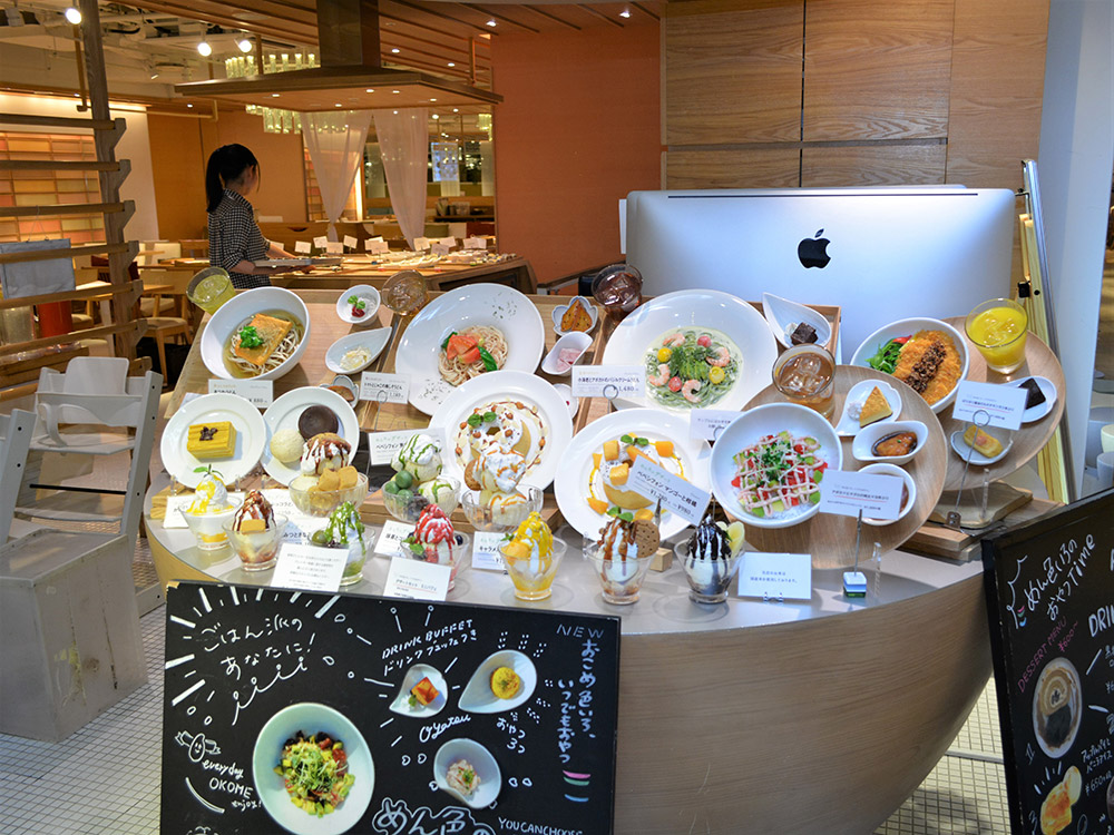 Round stand with pasta, dessert and drink replicas and chalkboards at a restaurant entrance