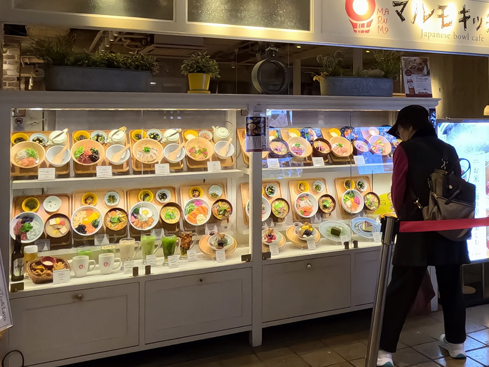 Rice bowl set meal replicas on wooden trays in a two-tier cafe display case